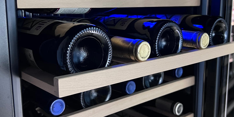 Wine bottles bathed in cool blue light within a wine refrigerator