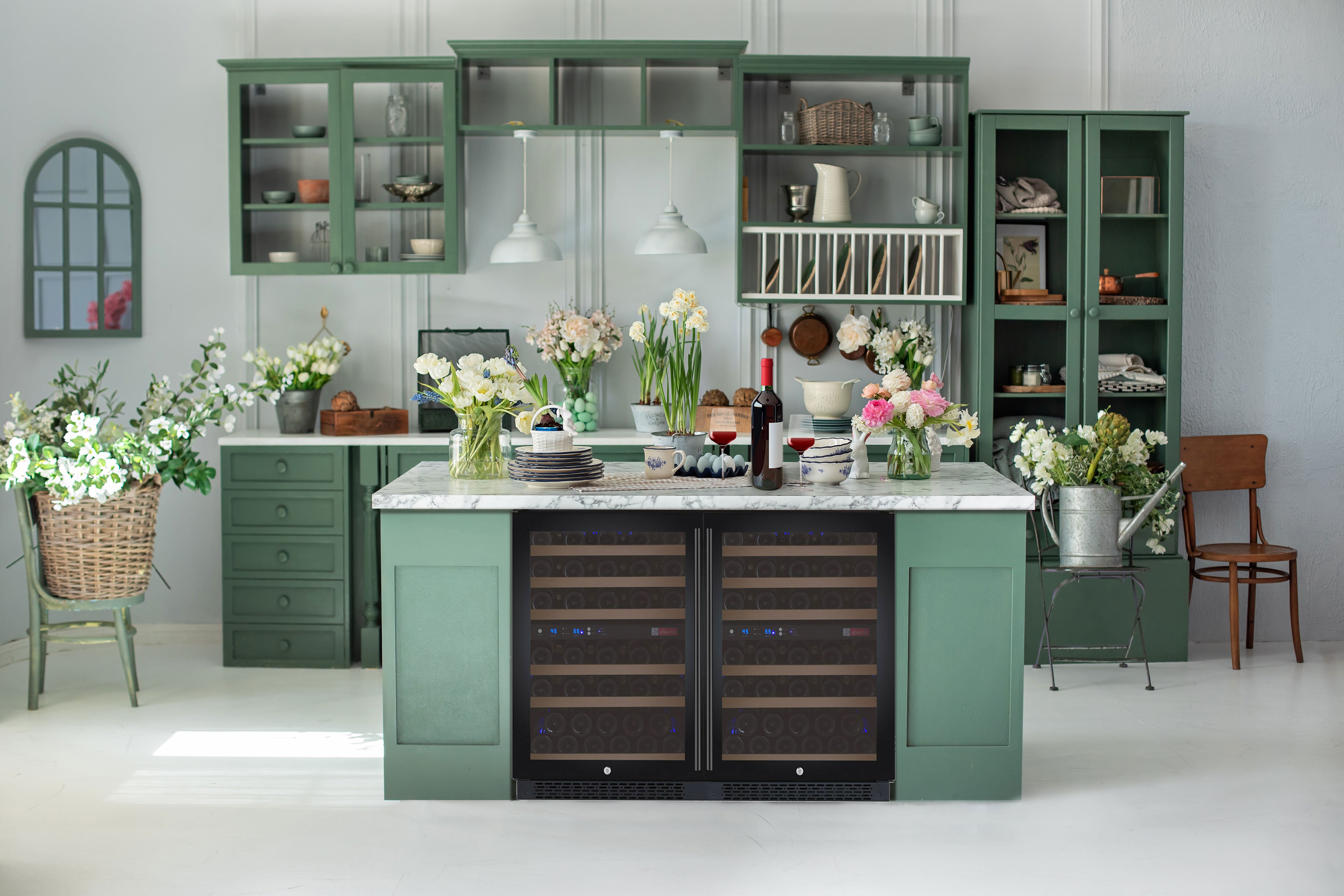 A pair of subtle black wine coolers are nestled unobtrusively under the countertop of a monochrome green kitchen